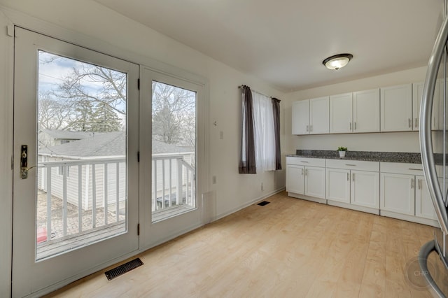 kitchen featuring light wood finished floors, visible vents, white cabinetry, baseboards, and stainless steel refrigerator