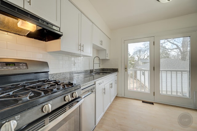 kitchen featuring stone counters, under cabinet range hood, a sink, visible vents, and stainless steel gas range