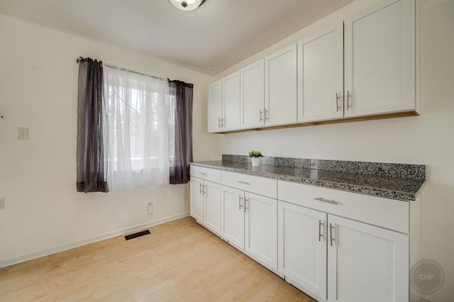 kitchen with light wood finished floors, baseboards, visible vents, white cabinets, and dark stone countertops