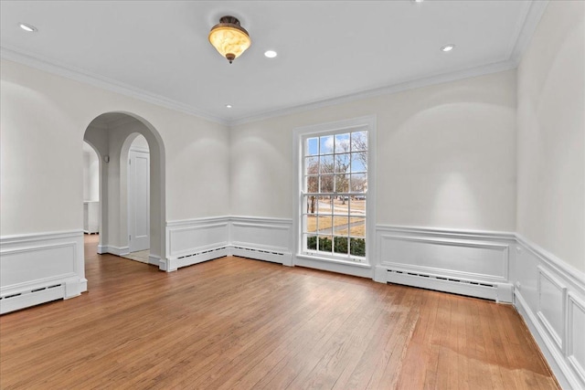 spare room featuring arched walkways, a baseboard radiator, recessed lighting, ornamental molding, and light wood finished floors