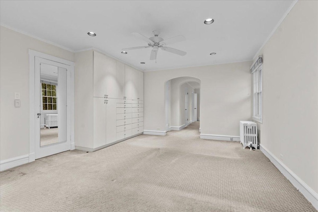 unfurnished room featuring arched walkways, radiator heating unit, and light colored carpet