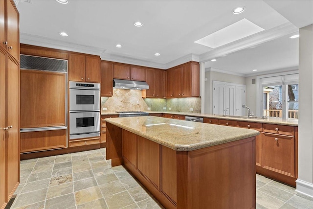 kitchen featuring a skylight, a kitchen island, stainless steel appliances, under cabinet range hood, and a sink