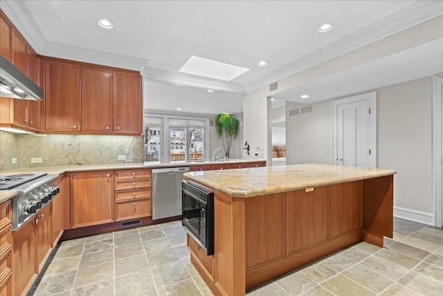 kitchen featuring a skylight, a center island, appliances with stainless steel finishes, light stone countertops, and tasteful backsplash