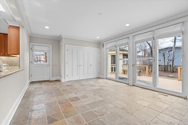 interior space with stone tile floors, baseboards, ornamental molding, a sink, and recessed lighting