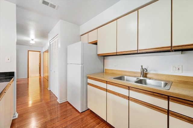 kitchen featuring light wood-style flooring, a sink, visible vents, white cabinetry, and freestanding refrigerator