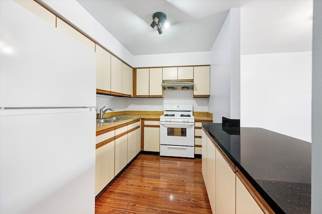 kitchen featuring white appliances, dark wood finished floors, cream cabinetry, under cabinet range hood, and a sink