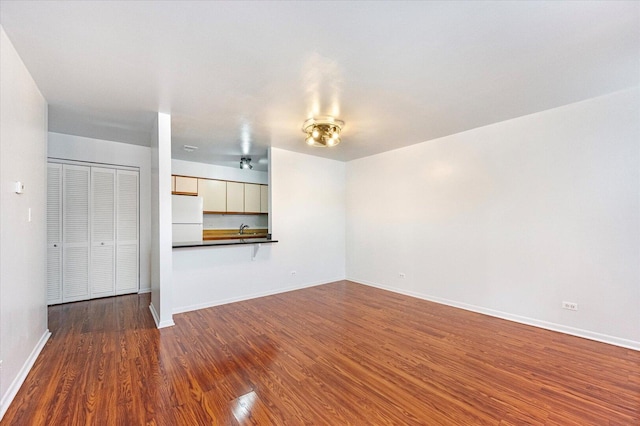 unfurnished living room with dark wood-style floors, a sink, and baseboards