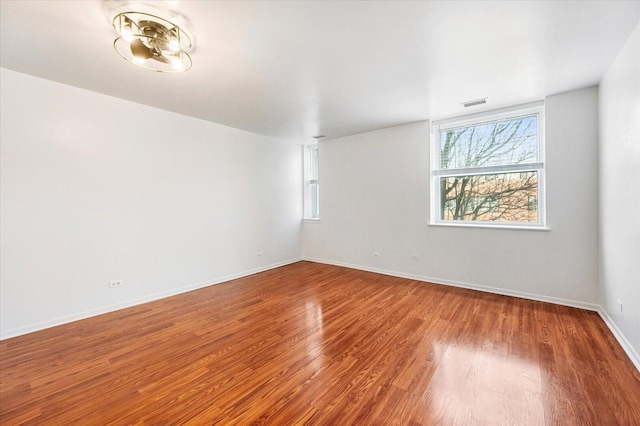 unfurnished room featuring baseboards, visible vents, and wood finished floors