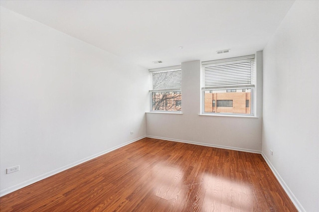 empty room featuring wood finished floors, visible vents, and baseboards