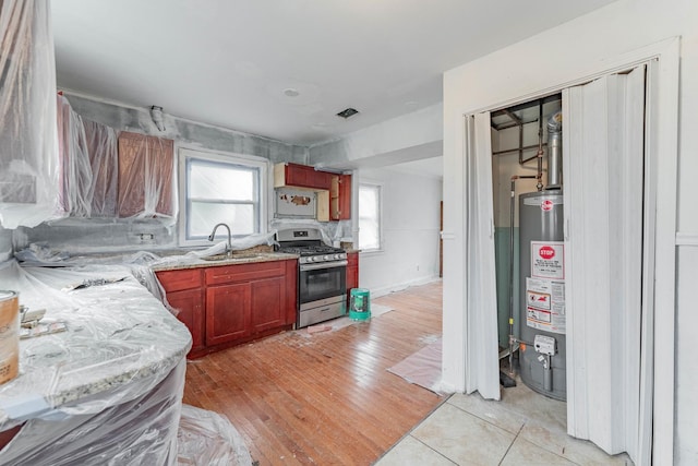 kitchen featuring light wood finished floors, gas range, a sink, light stone countertops, and gas water heater