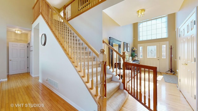 stairs with a towering ceiling, wood-type flooring, visible vents, and baseboards