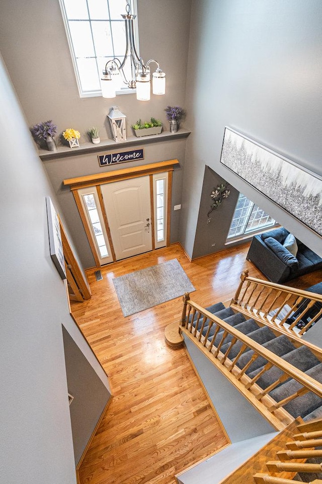 entryway with a chandelier, a wealth of natural light, a towering ceiling, and wood finished floors