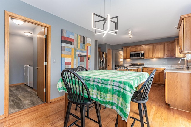 dining area with light wood-type flooring, washing machine and dryer, a chandelier, and baseboards