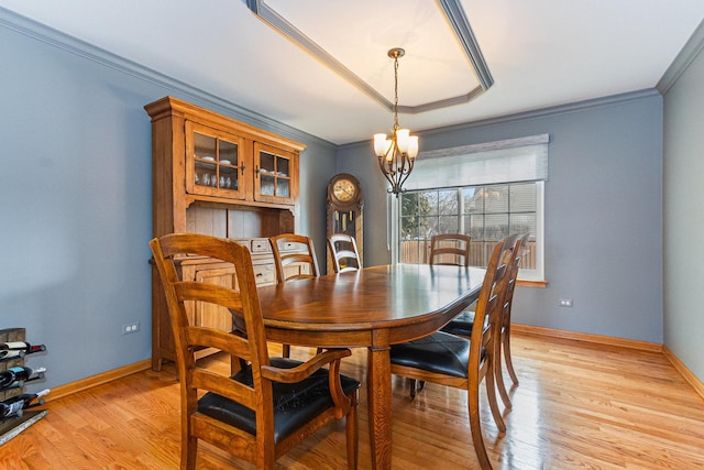 dining space featuring baseboards, light wood-style flooring, ornamental molding, an inviting chandelier, and a tray ceiling