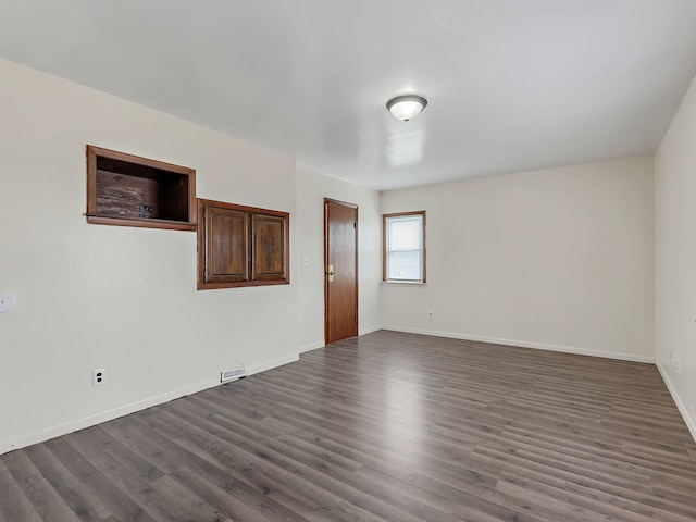 unfurnished room featuring visible vents, baseboards, and dark wood-type flooring