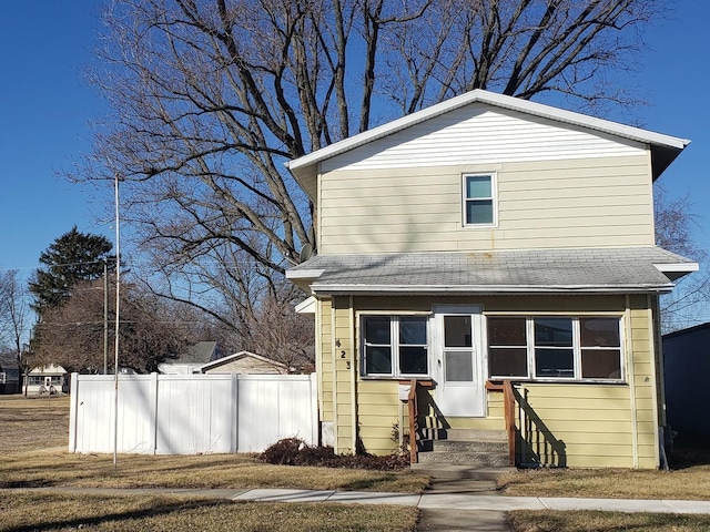 traditional-style home featuring entry steps, roof with shingles, and fence