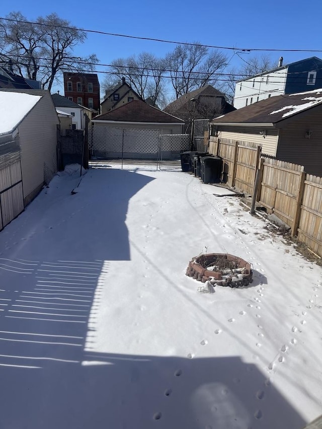 snowy yard featuring a fenced backyard, a detached garage, and a fire pit