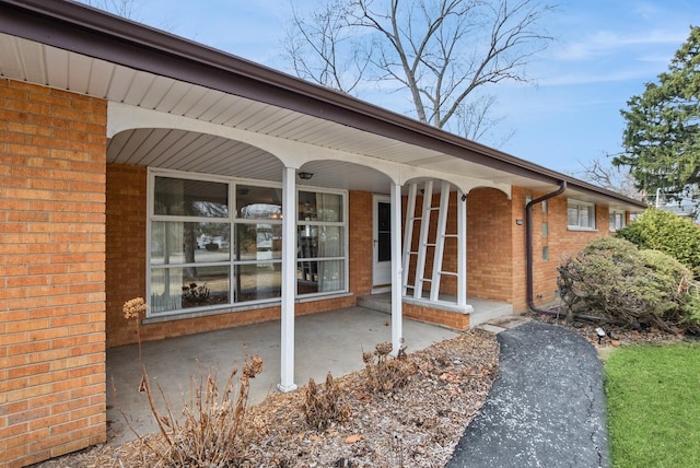 view of exterior entry featuring covered porch and brick siding