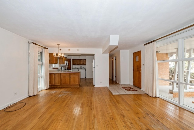 unfurnished living room with a chandelier, independent washer and dryer, light wood-style floors, and baseboards