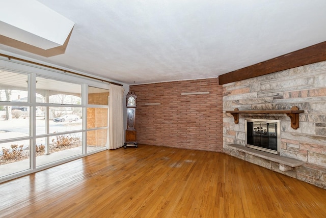 unfurnished living room with brick wall, a stone fireplace, and hardwood / wood-style flooring