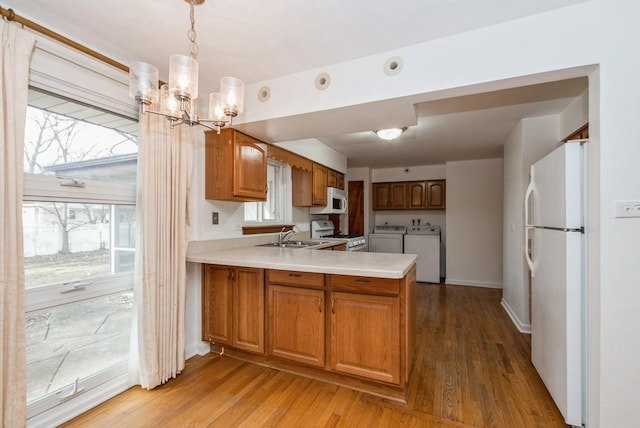 kitchen with white appliances, independent washer and dryer, a peninsula, light countertops, and a sink