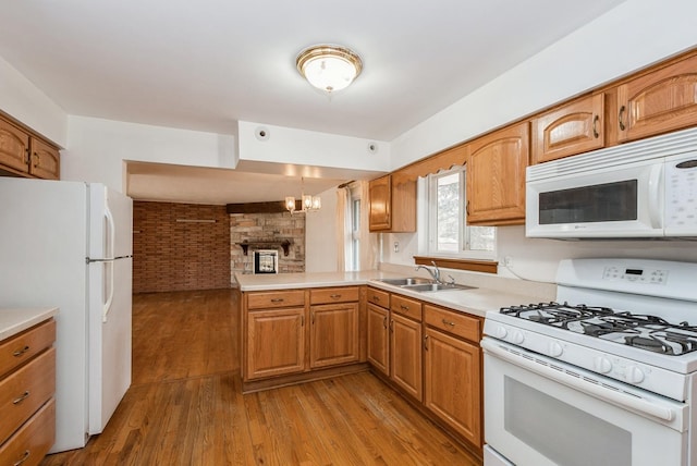 kitchen featuring a peninsula, white appliances, a sink, and light wood-style floors