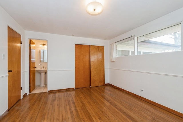 unfurnished bedroom featuring connected bathroom, a sink, wood finished floors, baseboards, and a closet