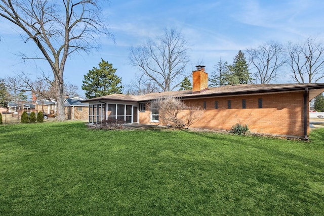 rear view of house featuring a sunroom, a chimney, brick siding, and a yard