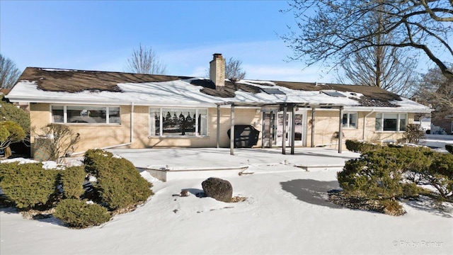 snow covered back of property with a chimney and brick siding