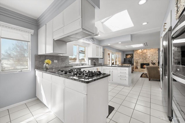 kitchen with a stone fireplace, light tile patterned flooring, a peninsula, stainless steel appliances, and white cabinets