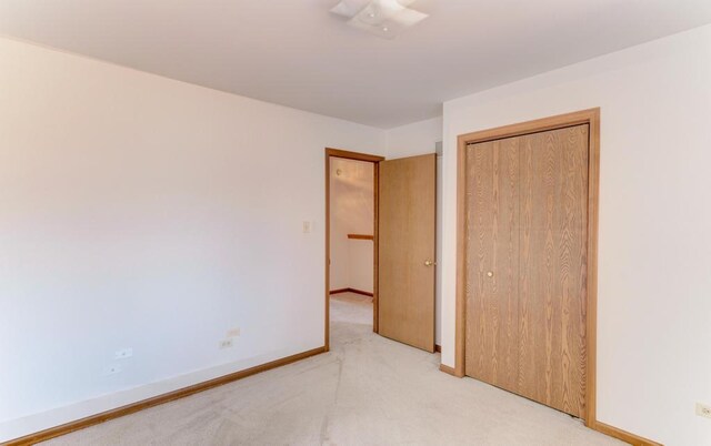 unfurnished bedroom featuring light colored carpet, baseboards, and a closet