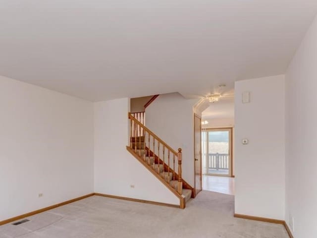 empty room featuring visible vents, light carpet, baseboards, and stairs