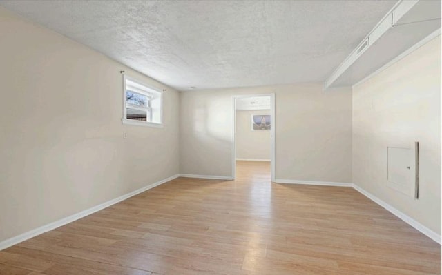 spare room featuring baseboards, light wood-type flooring, and a textured ceiling