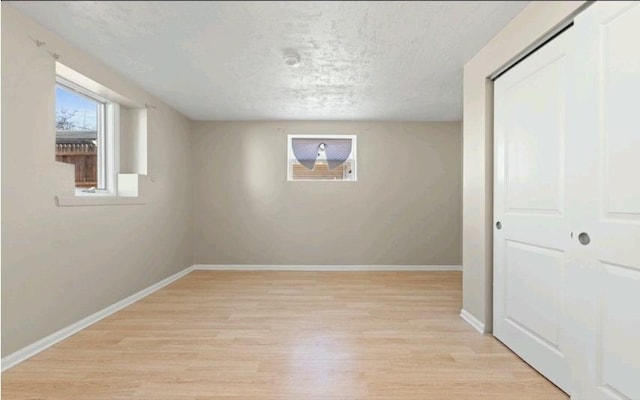 basement featuring light wood finished floors, a textured ceiling, and baseboards