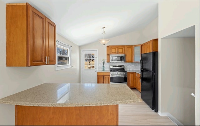 kitchen with vaulted ceiling, light stone counters, brown cabinets, appliances with stainless steel finishes, and a peninsula