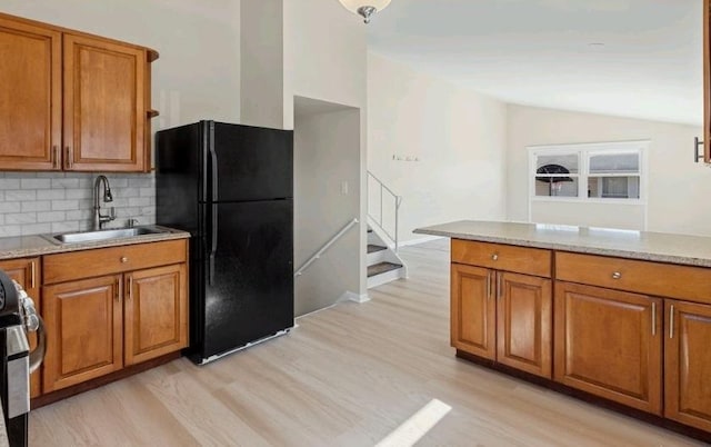 kitchen featuring vaulted ceiling, brown cabinets, freestanding refrigerator, and a sink