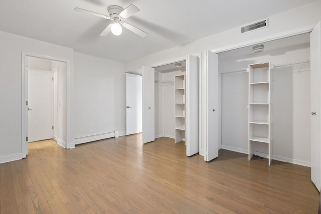 unfurnished bedroom with wood finished floors, visible vents, ceiling fan, multiple closets, and a baseboard heating unit