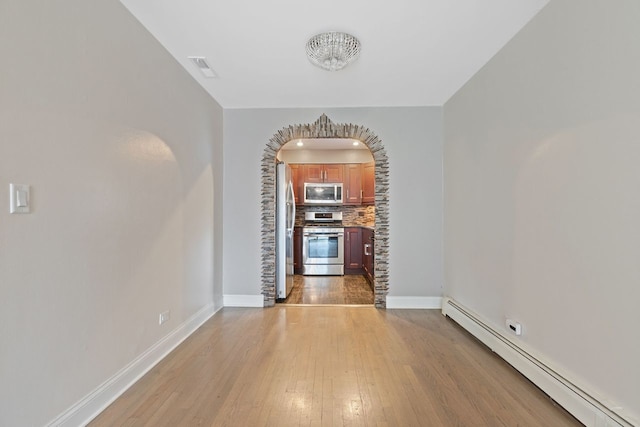 unfurnished dining area featuring visible vents, baseboards, arched walkways, light wood-style floors, and a baseboard heating unit