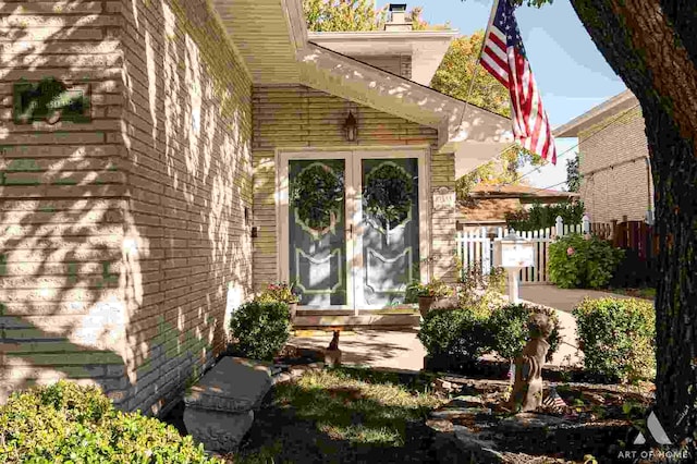 property entrance with brick siding, a chimney, fence, and french doors