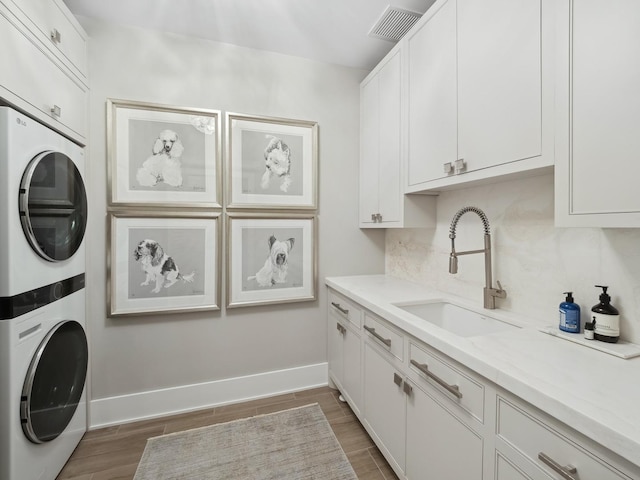 laundry area featuring light wood finished floors, baseboards, cabinet space, stacked washer / drying machine, and a sink