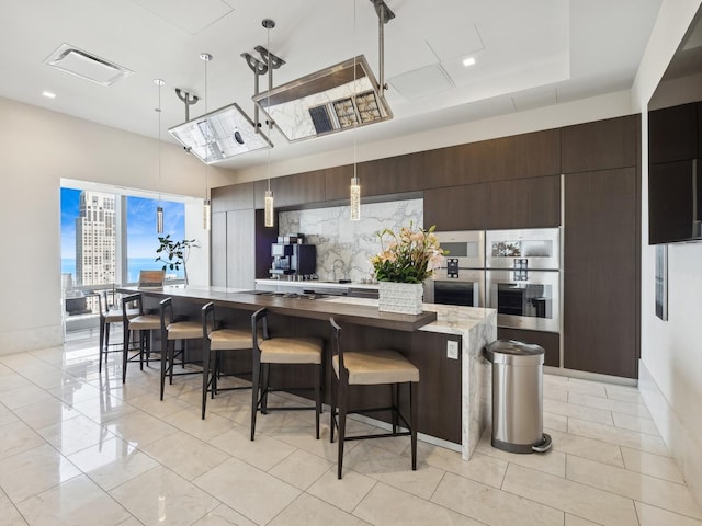 kitchen featuring a breakfast bar area, visible vents, hanging light fixtures, a large island, and decorative backsplash