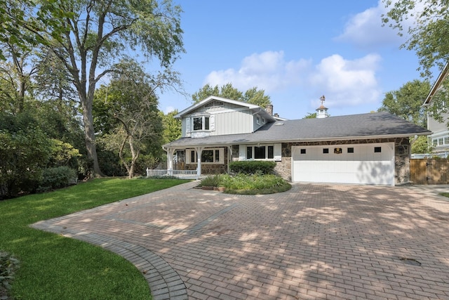 traditional home with stone siding, an attached garage, fence, decorative driveway, and a front yard