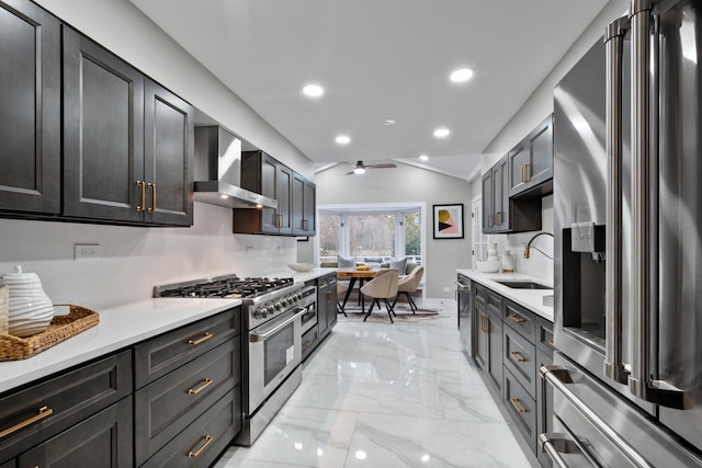 kitchen with a sink, high quality appliances, marble finish floor, light countertops, and wall chimney range hood