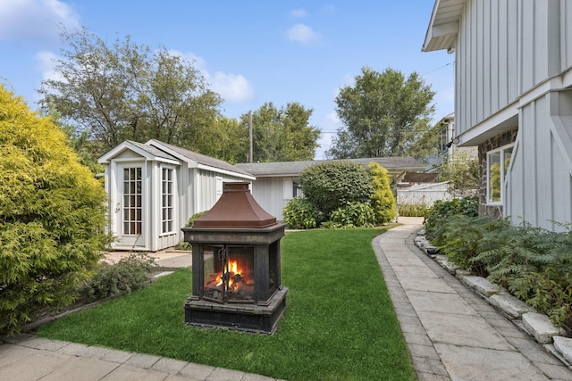 view of yard featuring a warm lit fireplace, fence, and an outdoor structure