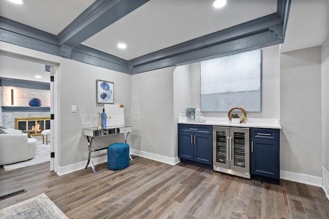 bar with dark wood-style floors, a fireplace, a bar, beverage cooler, and baseboards