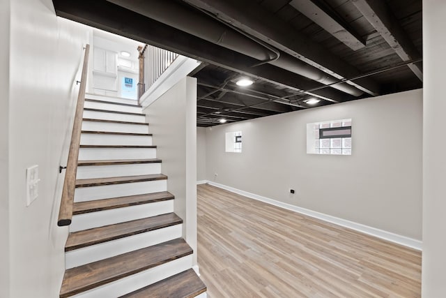 basement featuring baseboards, stairs, and light wood-style floors