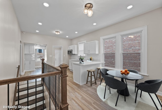 kitchen featuring tasteful backsplash, white cabinets, light wood-style flooring, stainless steel microwave, and light countertops