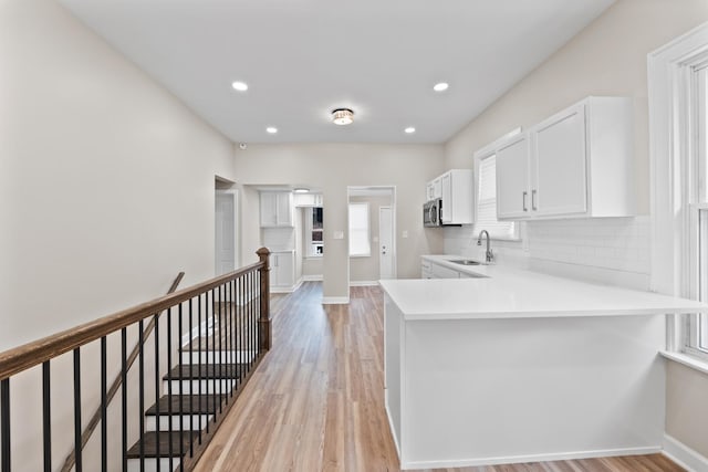 kitchen featuring a peninsula, white cabinets, light countertops, and decorative backsplash