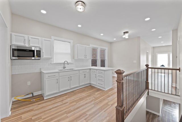 kitchen featuring light wood-style flooring, a sink, white cabinetry, light countertops, and stainless steel microwave