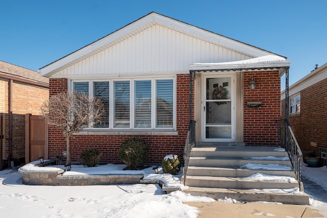 bungalow-style house featuring entry steps, fence, and brick siding